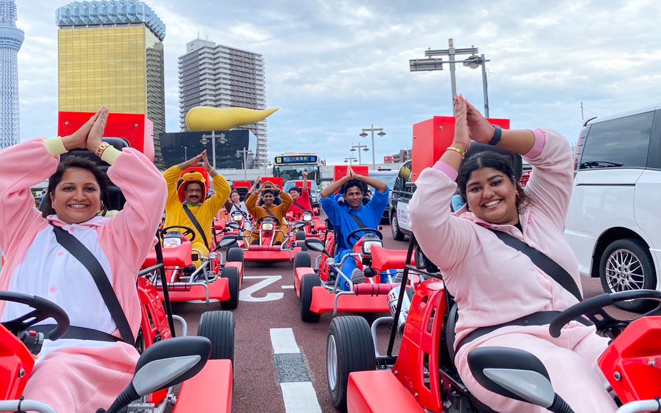Go-kart riders in costumes on Tokyo Asakusa street with cityscape backdrop.