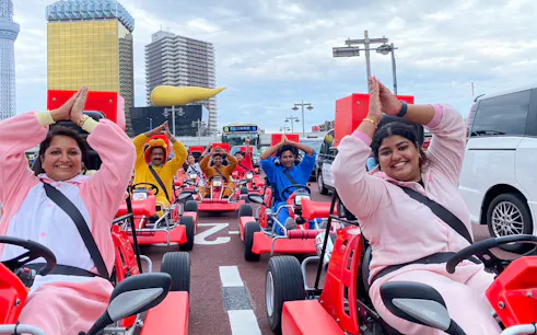 Go-kart riders in costumes on Tokyo Asakusa street with cityscape backdrop.