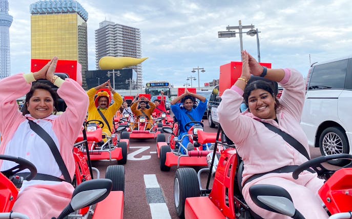 Go-kart riders in costumes on Tokyo Asakusa street with cityscape backdrop.