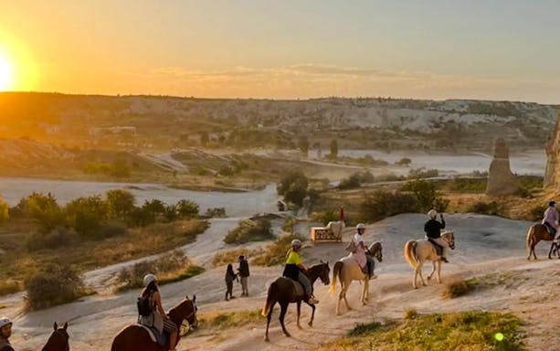 Guests horseback riding at sunrise in Cappadocia's scenic landscape.