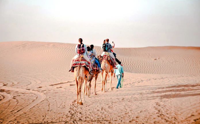 Camel trekking tour in Abu Dhabi desert with riders on camels.