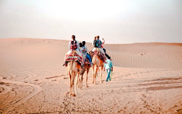 Camel trekking tour in Abu Dhabi desert with riders on camels.