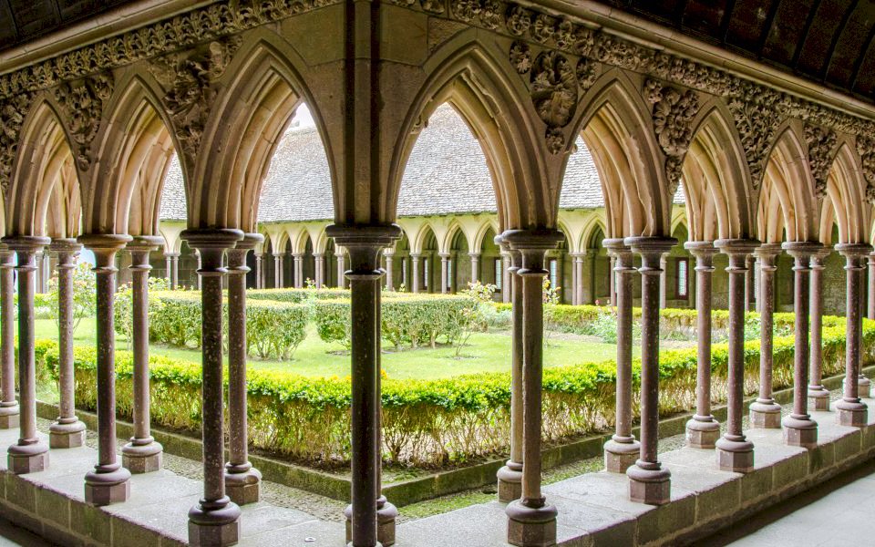 Cloister arches at Mont-Saint-Michel Abbey, France, overlooking a garden courtyard.