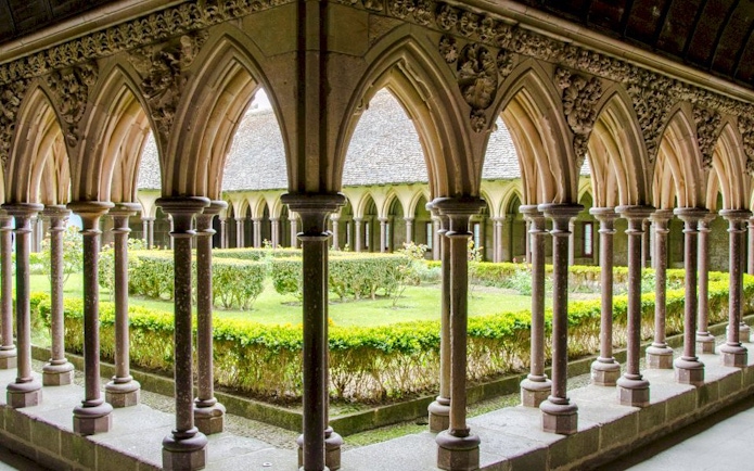 Cloister arches at Mont-Saint-Michel Abbey, France, overlooking a garden courtyard.