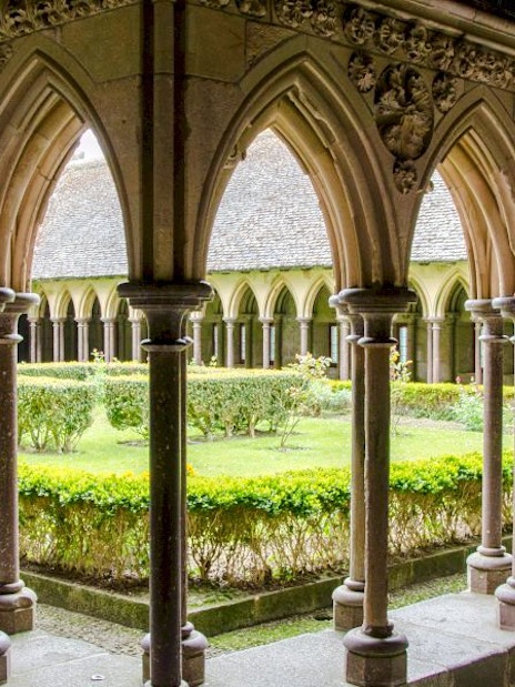 Cloister arches at Mont-Saint-Michel Abbey, France, overlooking a garden courtyard.