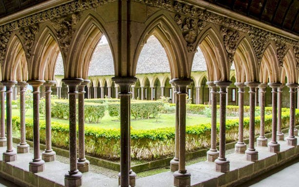 Cloister arches at Mont-Saint-Michel Abbey, France, overlooking a garden courtyard.