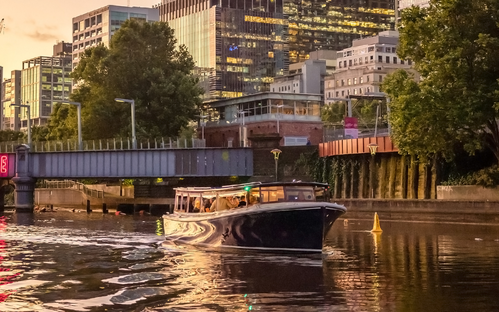 Cruise boat on Yarra River at sunset with Melbourne cityscape in background.