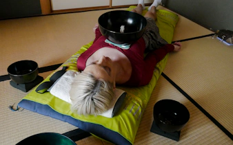 Person experiencing a Japanese sound bath with bowls on a tatami mat in Kyoto.