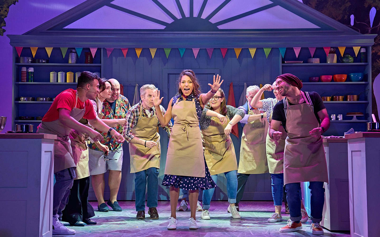 Performers in aprons on stage during The Great British Bake Off Musical.