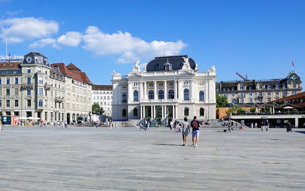 Zürich Opera House with people walking in Sechseläutenplatz on a sunny day.