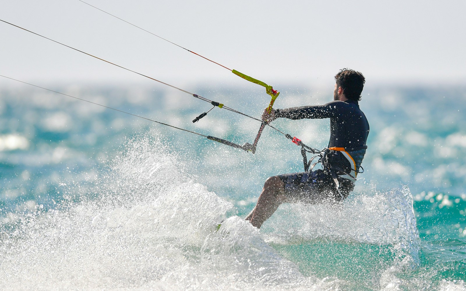 Man kiteboarding with safety harness on ocean wave.