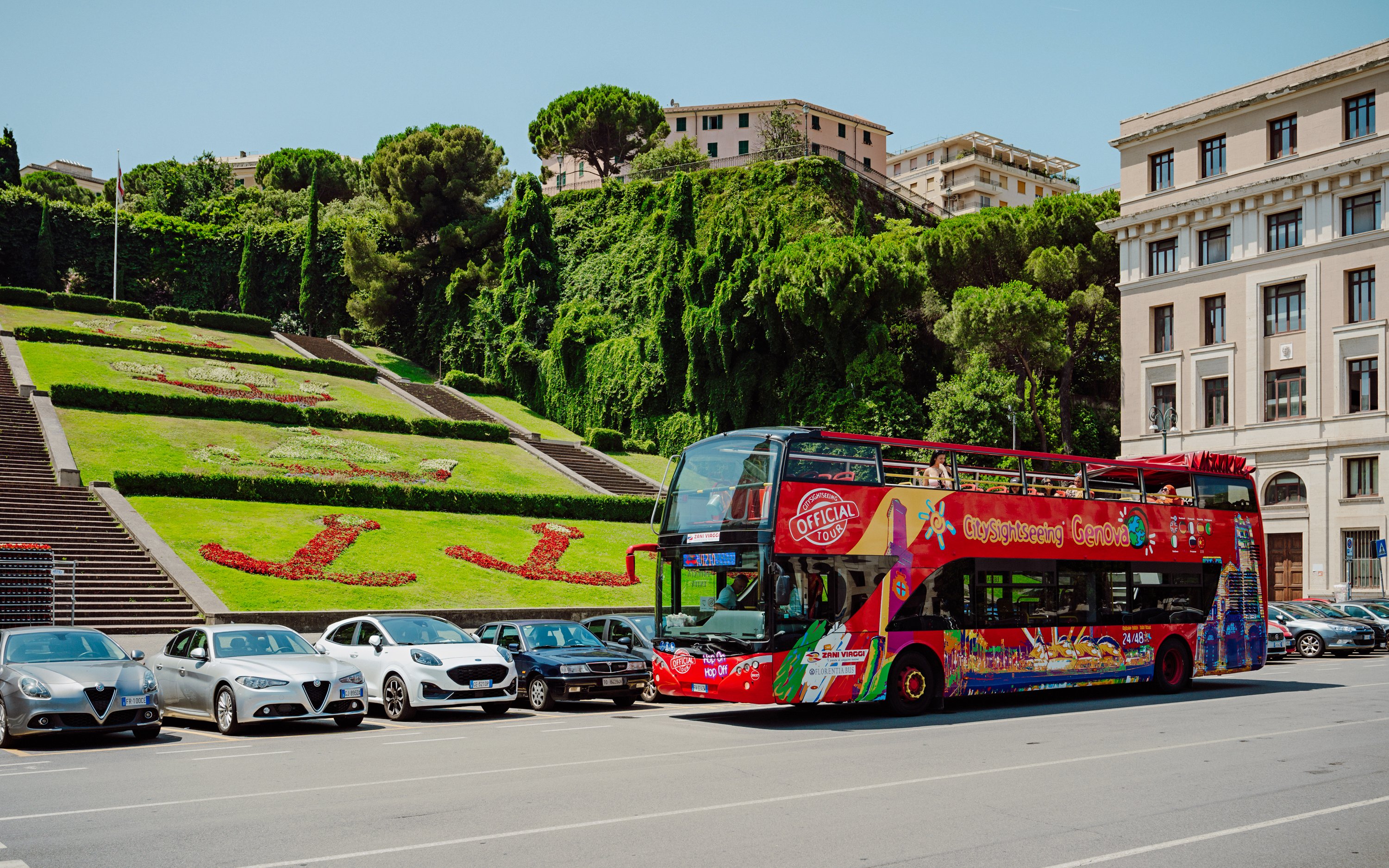 City Sightseeing bus parked near floral display in Genova, Italy.