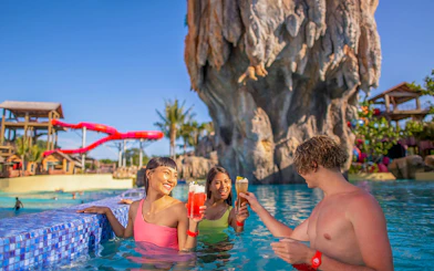 People enjoying drinks in the pool at Wave Bar, Andamanda Phuket, with a waterslide in the background.