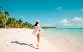 Woman walking on Saona Island beach, Dominican Republic, with palm trees and turquoise water.