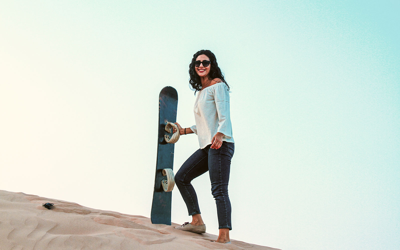 Woman holding sandboard on dune in Abu Dhabi desert.