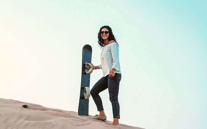 Woman holding sandboard on dune in Abu Dhabi desert.
