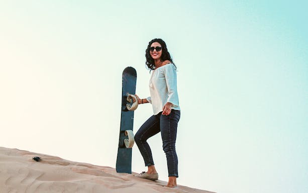 Woman holding sandboard on dune in Abu Dhabi desert.