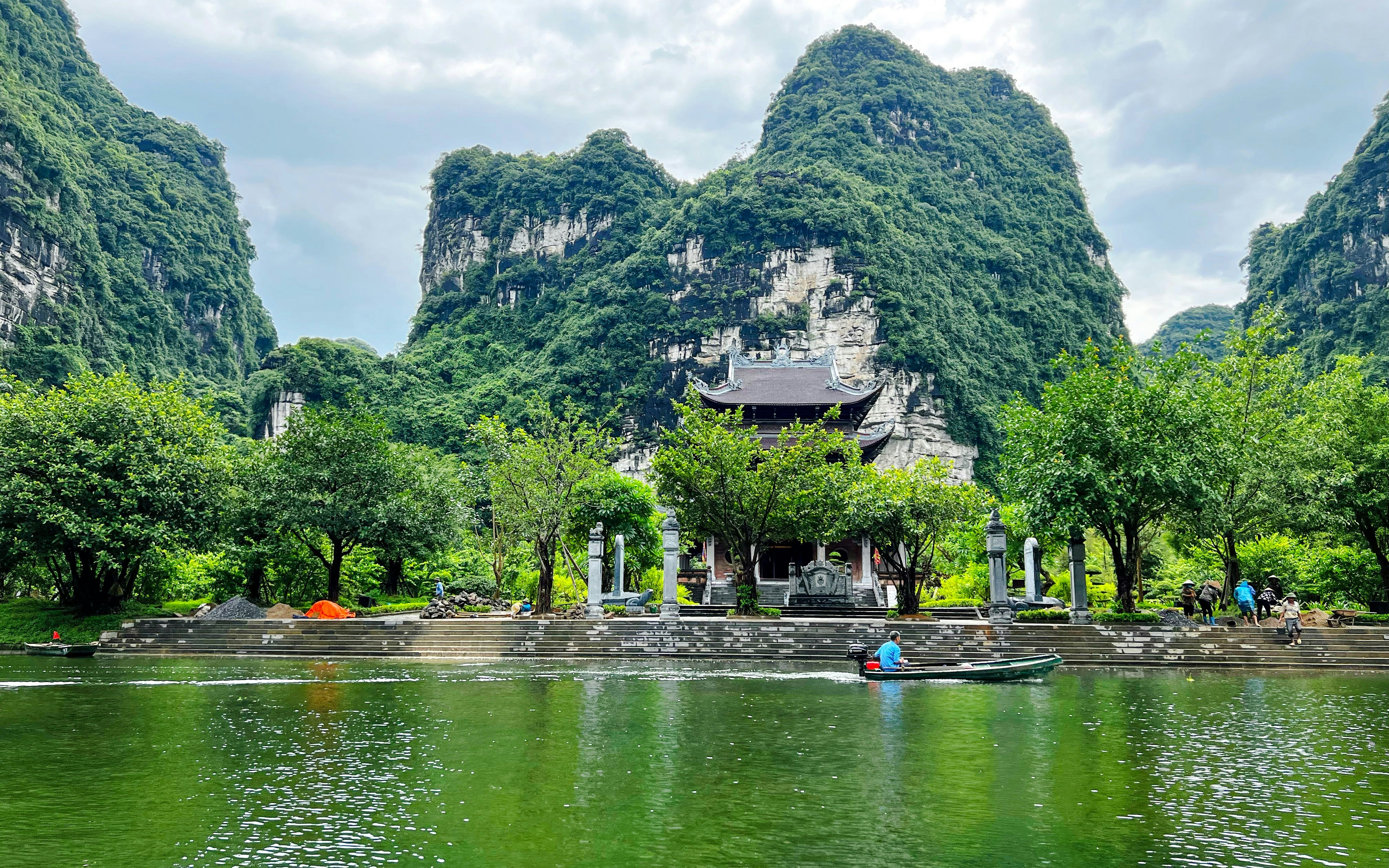 Boat on Trang An Waterways with lush limestone mountains and temple in Vietnam.