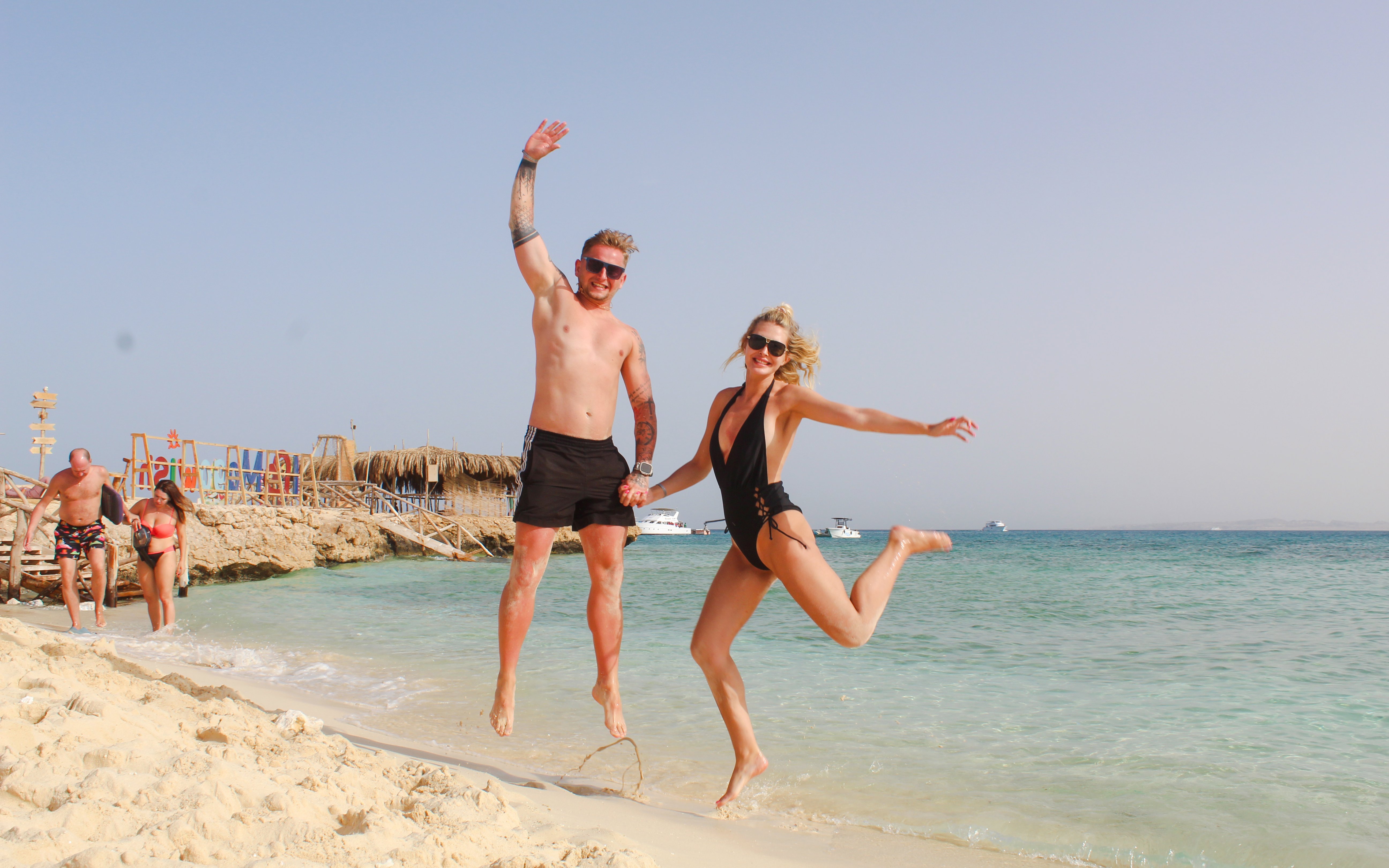 Couple jumping on sandy beach during Giftun 3 Islands Tour with clear blue water in background.