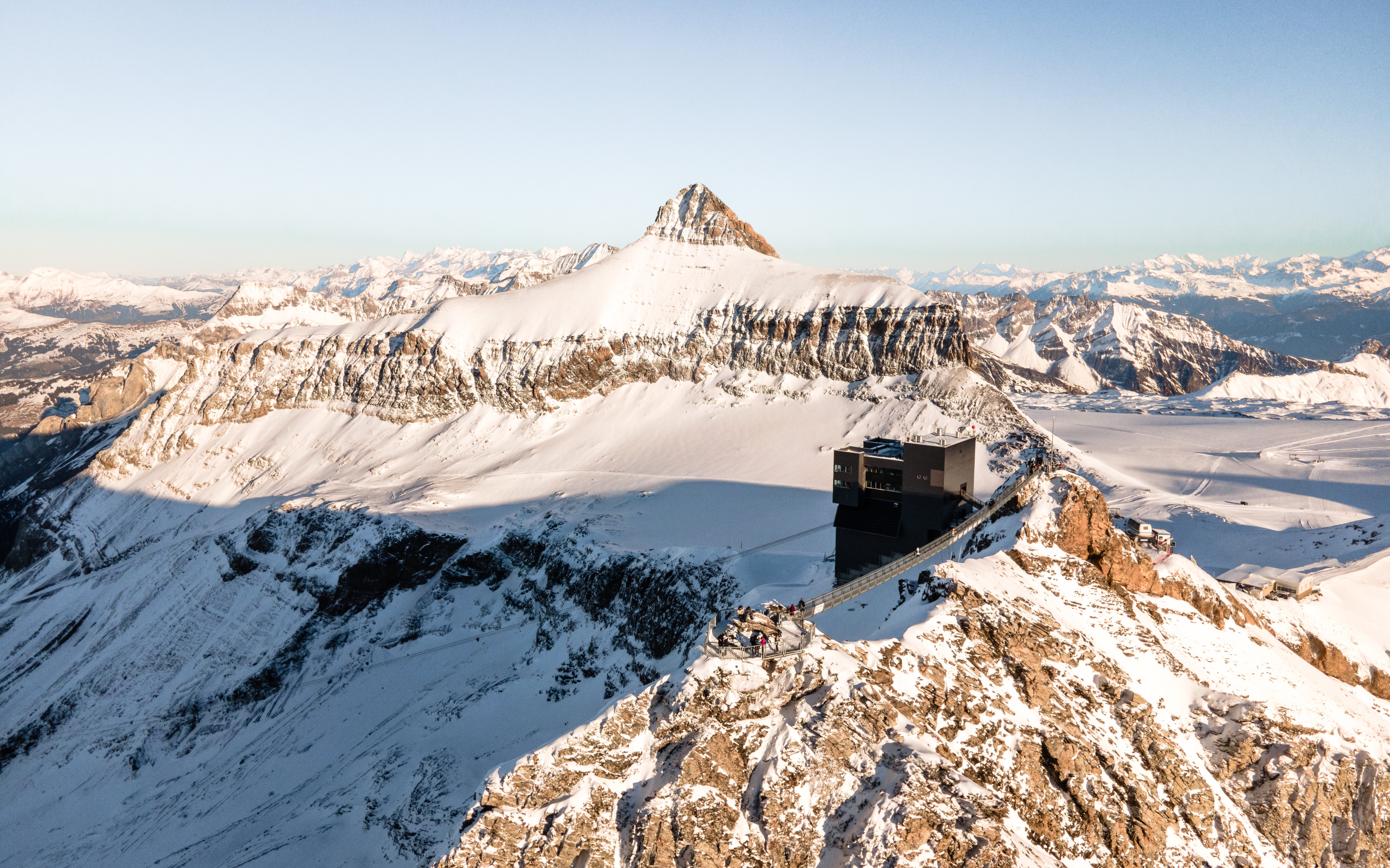 Aerial view of Glacier 3000 in Switzerland with a restaurant overlooking snow-covered peaks.