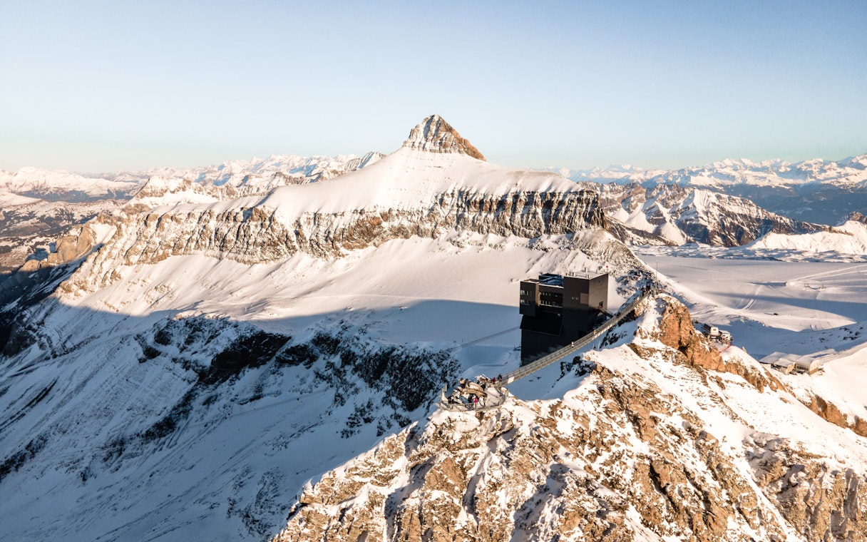 Aerial view of Glacier 3000 in Switzerland with a restaurant overlooking snow-covered peaks.