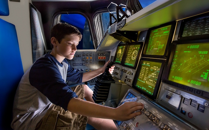Boy operating controls inside Space Shuttle Atlantis simulator.