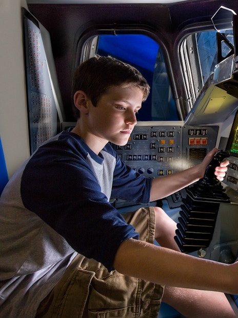 Boy operating controls inside Space Shuttle Atlantis simulator.