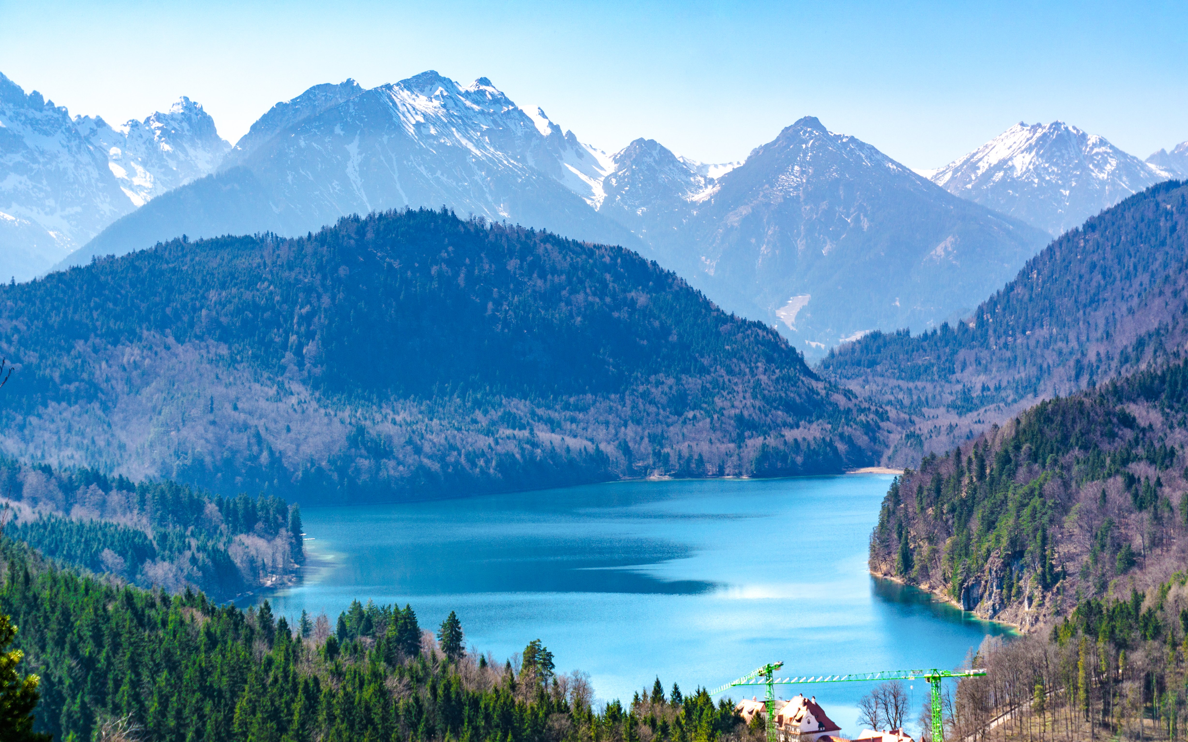 Alpsee Lake surrounded by forested hills and snow-capped mountains in Bavaria, Germany.