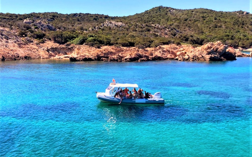 Boat tour near Capo Figari with tourists, clear blue water, and rocky coastline.
