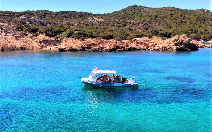 Boat tour near Capo Figari with tourists, clear blue water, and rocky coastline.