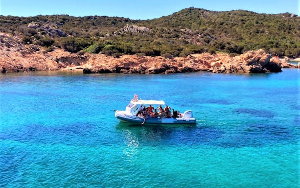 Boat tour near Capo Figari with tourists, clear blue water, and rocky coastline.