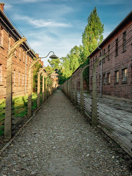 Pathway between brick buildings and barbed wire fences at Auschwitz, Poland.