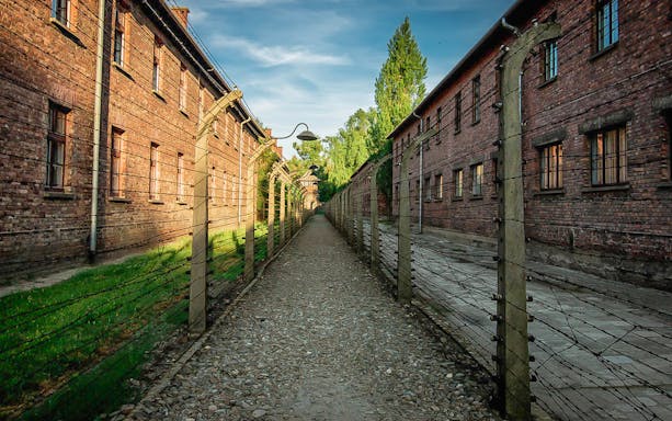 Pathway between brick buildings and barbed wire fences at Auschwitz, Poland.