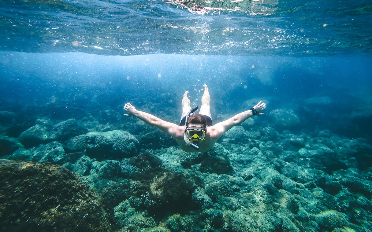 Snorkeler exploring underwater rocks in Santorini during catamaran cruise.
