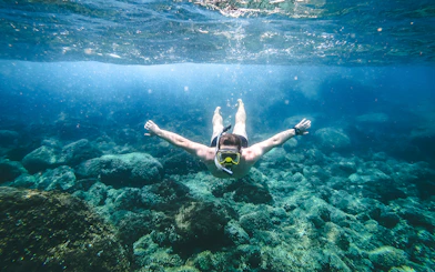 Snorkeler exploring underwater rocks in Santorini during catamaran cruise.