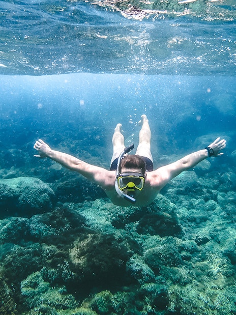 Snorkeler exploring underwater rocks in Santorini during catamaran cruise.