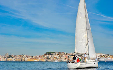 Sailboat on Tagus River with Lisbon cityscape in background.