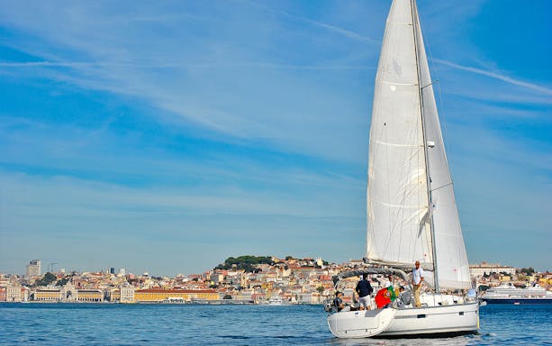 Sailboat on Tagus River with Lisbon cityscape in background.
