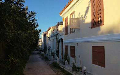 Narrow street in Plaka, Athens with traditional buildings and greenery, part of self-guided city exploration game.