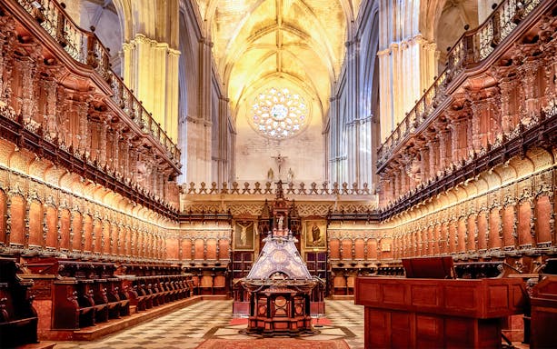 Seville Cathedral interior with ornate wooden choir stalls and vaulted ceiling.