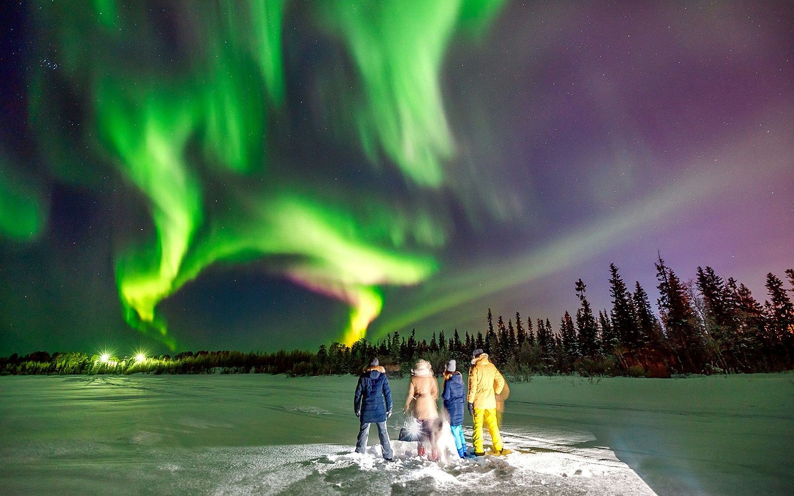Tourists watching Northern Lights on a snowy landscape during a small group tour.