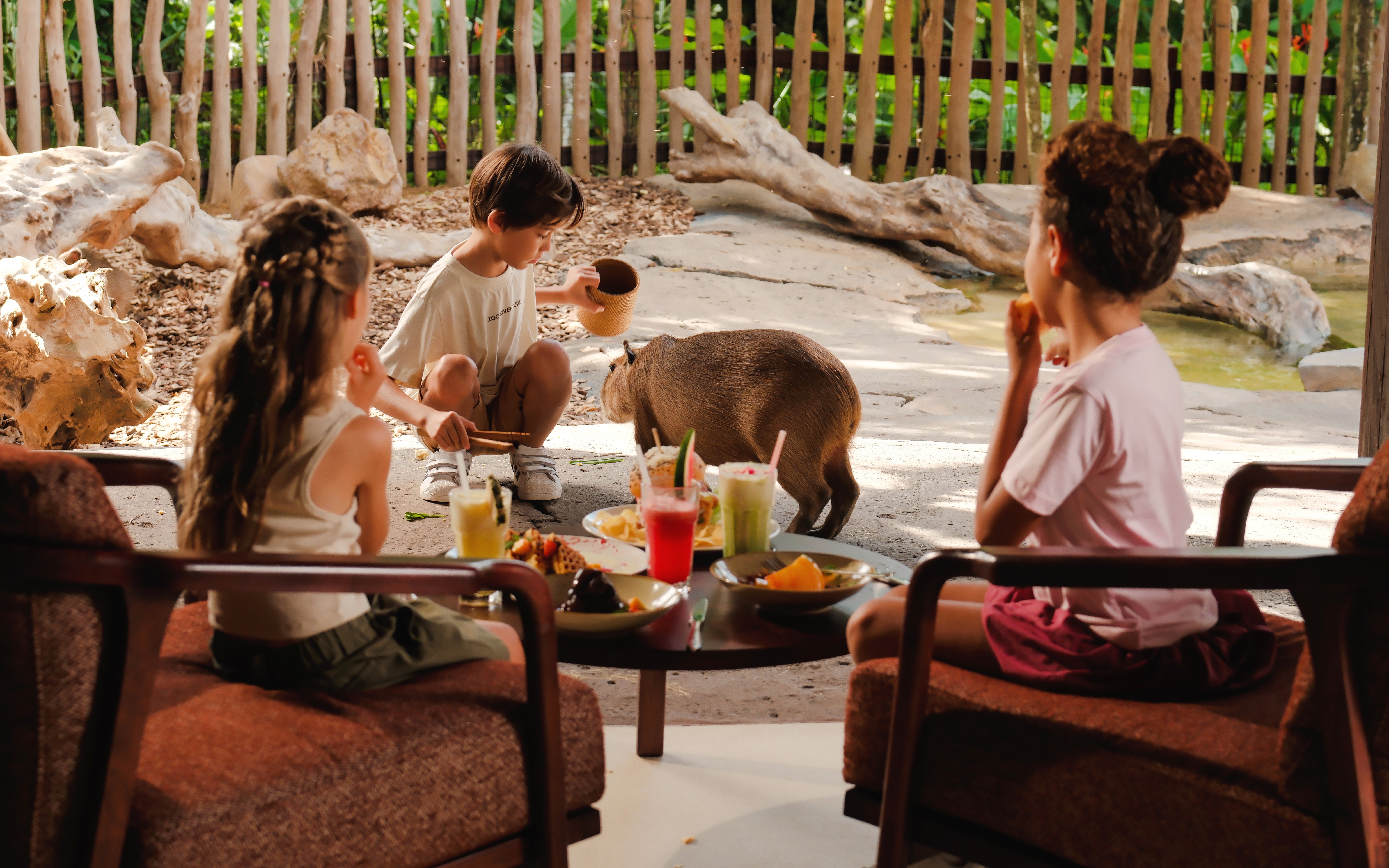 Children interacting with a capybara at Bali Zoo, with brunch on the table.
