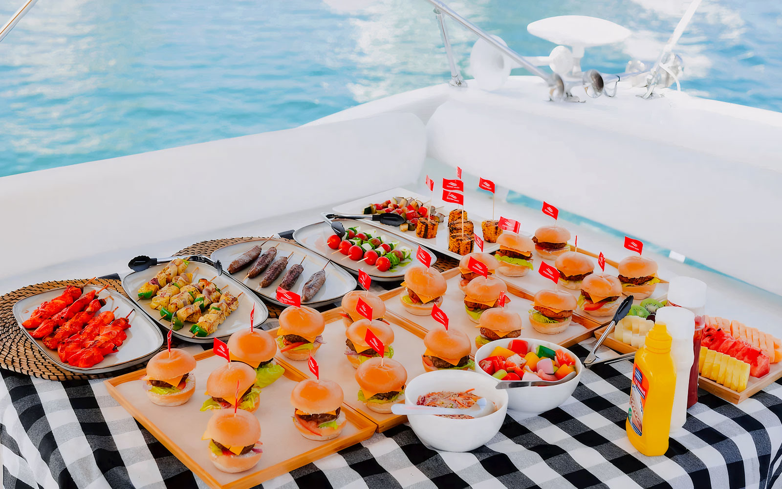 Assorted gourmet meals on a luxury yacht in Dubai, featuring sliders, skewers, and fresh fruit.