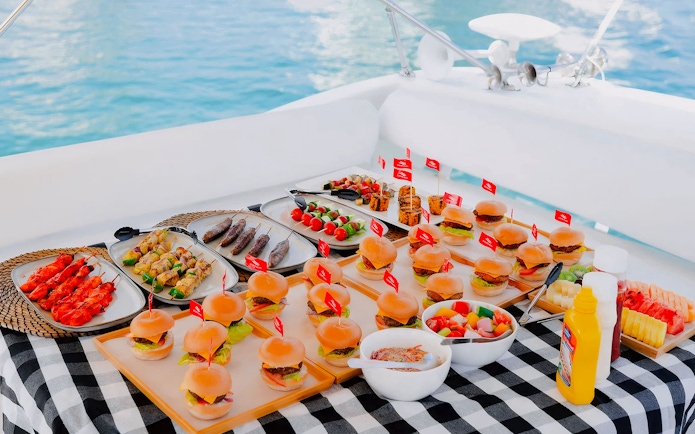 Assorted gourmet meals on a luxury yacht in Dubai, featuring sliders, skewers, and fresh fruit.