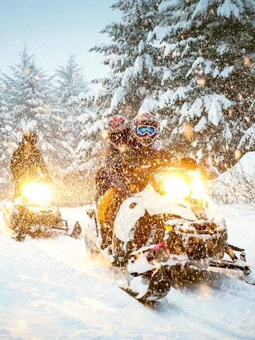 Snowmobile riders navigating snowy forest trail.