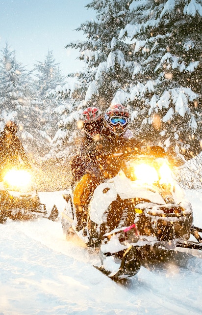 Snowmobile riders navigating snowy forest trail.