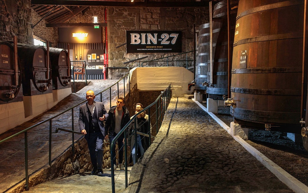 Visitors touring Fonseca Port Wine Cellars, passing large wooden barrels.