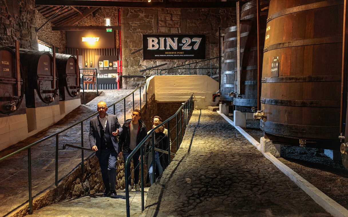 Visitors touring Fonseca Port Wine Cellars, passing large wooden barrels.