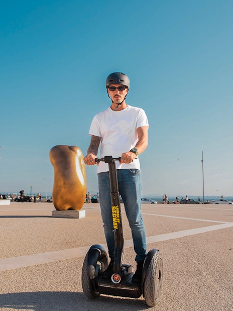 Person on Segway in Lisbon's Alfama district near sculptures and historic architecture.