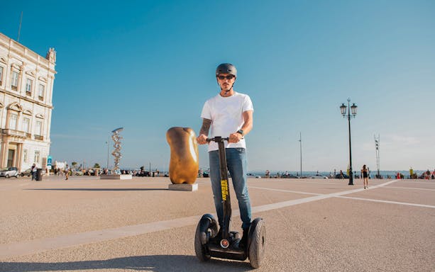 Person on Segway in Lisbon's Alfama district near sculptures and historic architecture.